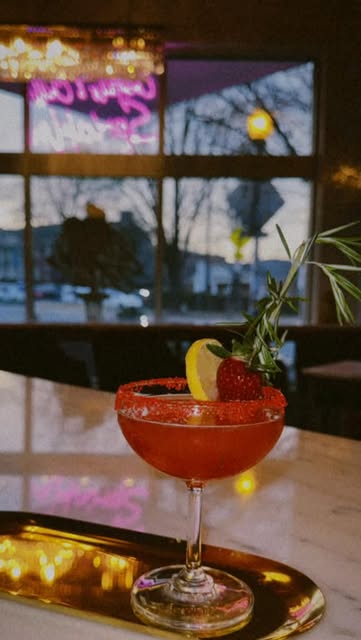 Sugar-rimmed red cocktail with strawberry and lemon garnish on the marble bar
